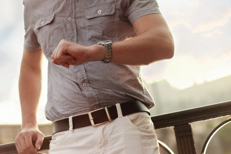 man-leaning-against-railing-and-checking-watch